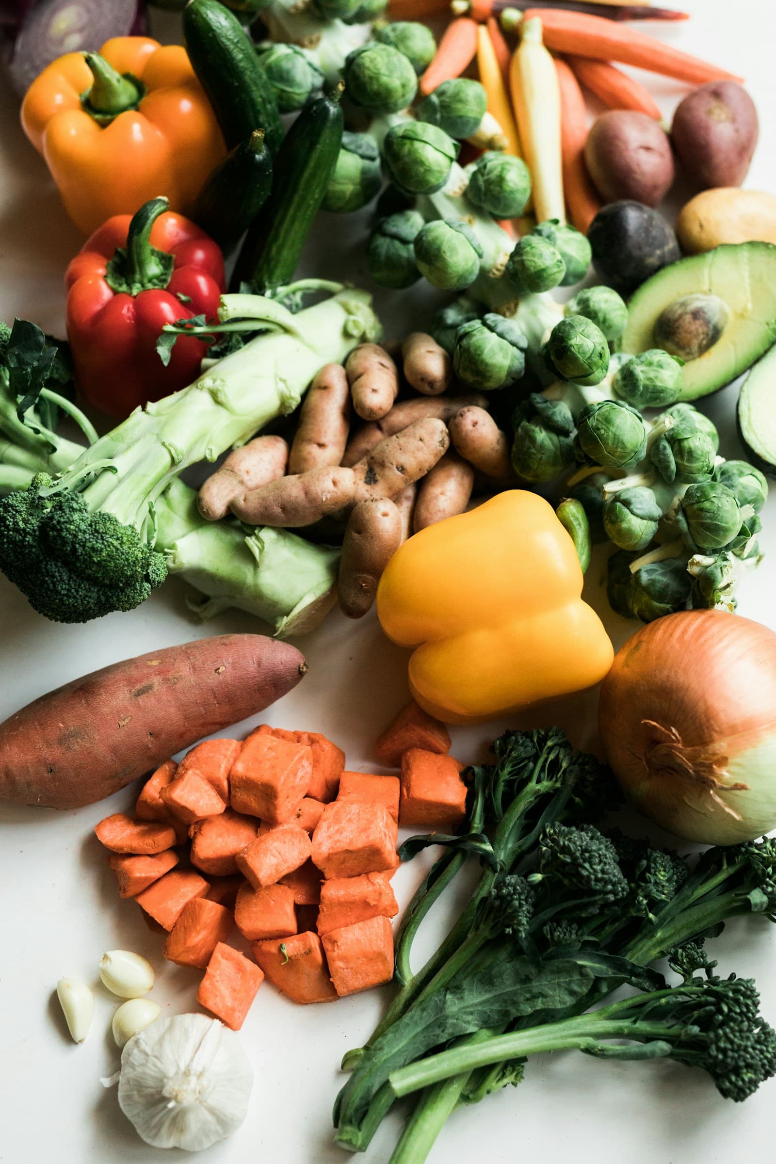 Fresh broccoli, peppers, Brussels sprouts and potatoes laid out on a white surface